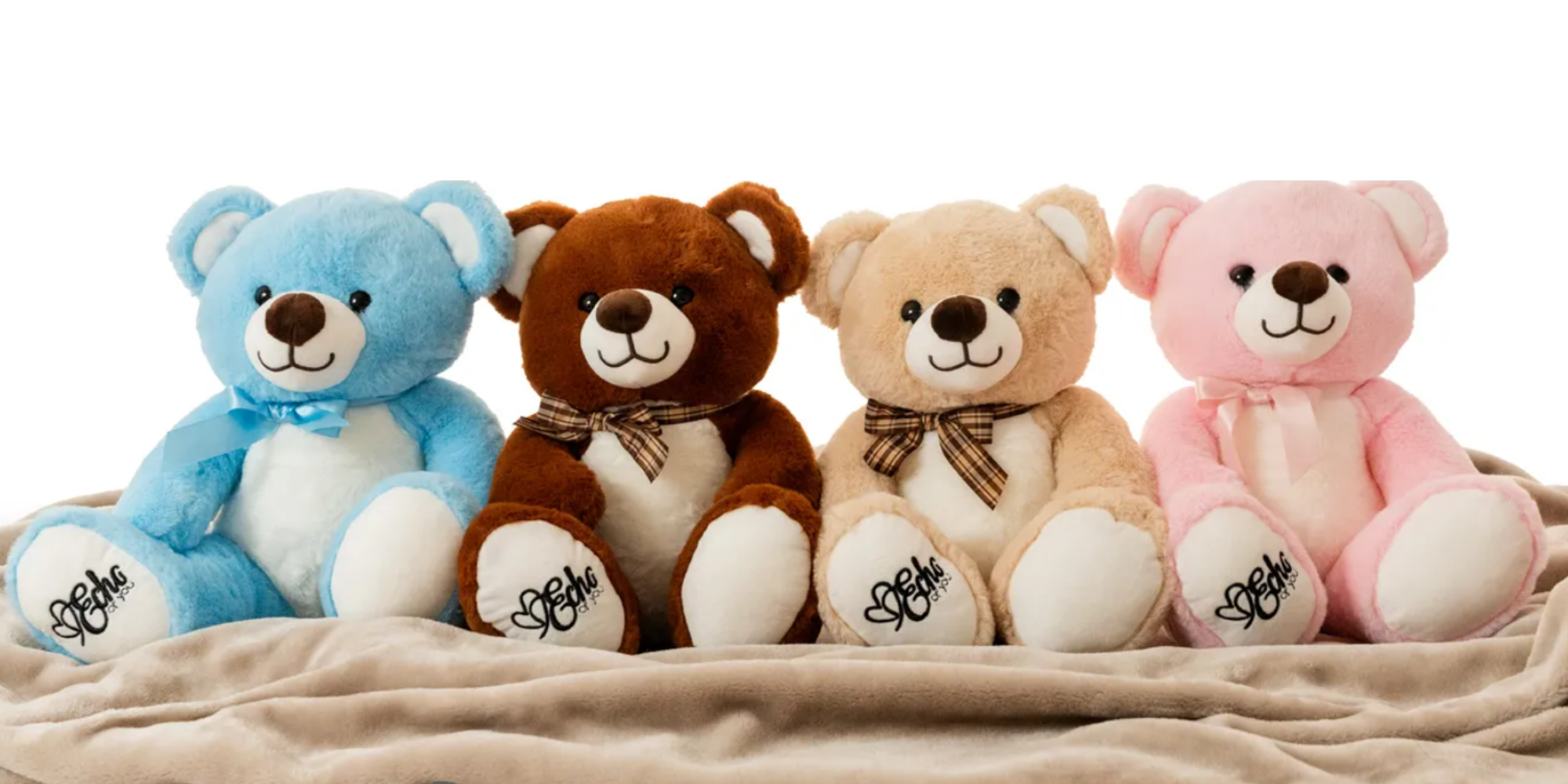 Four teddy bears in blue, brown, beige, and pink sitting on a beige blanket.